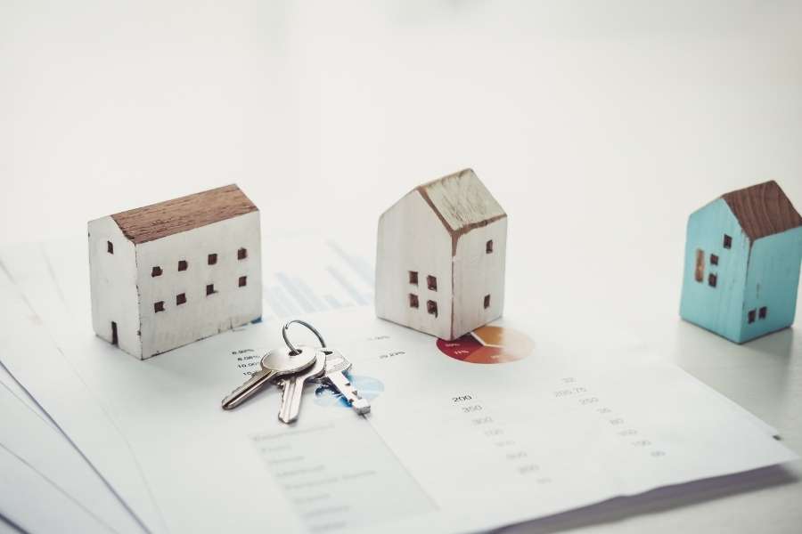 Des maquettes de maisons et un trousseau de clés reposent sur des documents financiers avec des graphiques, symbolisant des investisseurs rentables.