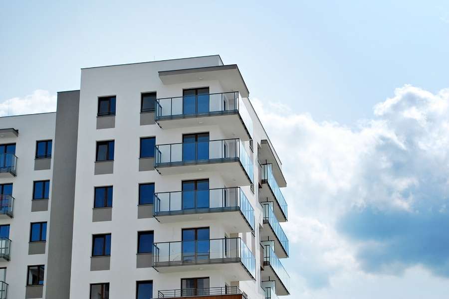 Un grand immeuble résidentiel moderne avec de nombreux balcons sous un ciel partiellement nuageux, illustrant la problématique d'une passoire thermique.