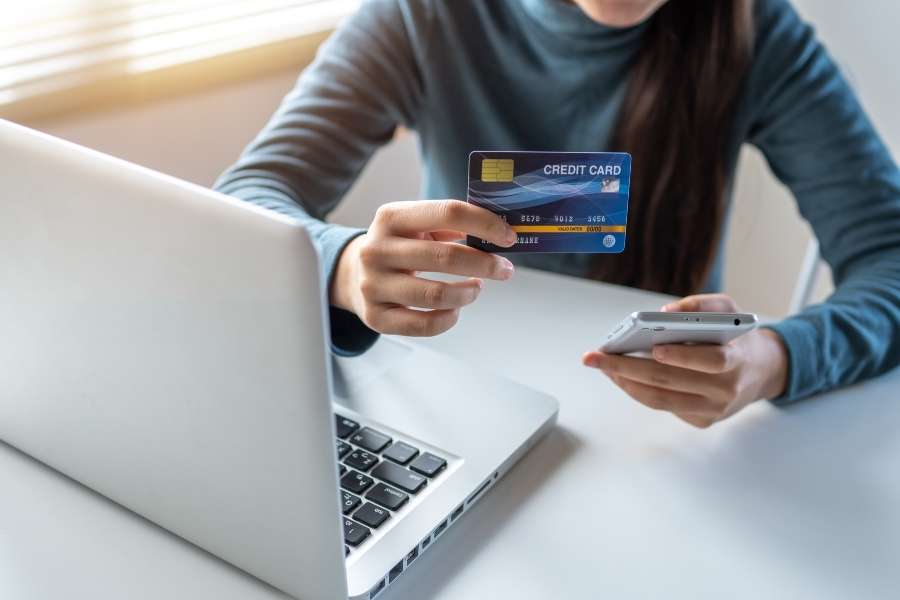 Une personne tient une carte bancaire et un smartphone pour gérer un rachat de crédit en ligne.